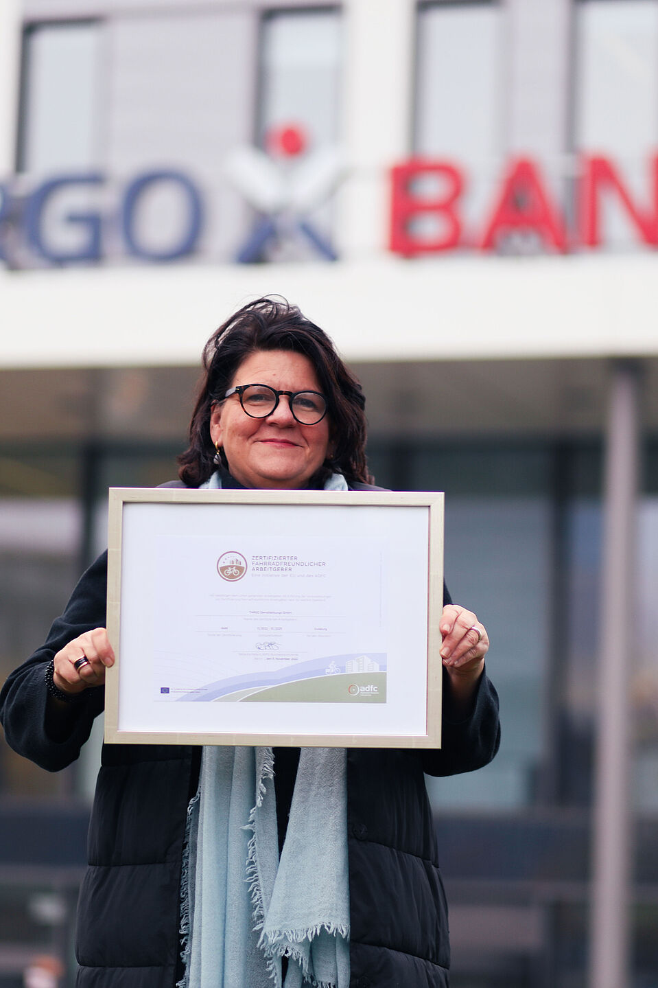 Birgit Kind vom TARGOBANK-Einkauf freut sich über die Zertifizierung Birgit Kind von der TARGOBANK in Duisburg vor dem Bankgebäude mit einer Urkunde für Fahrradförderung in ihrem Betrieb