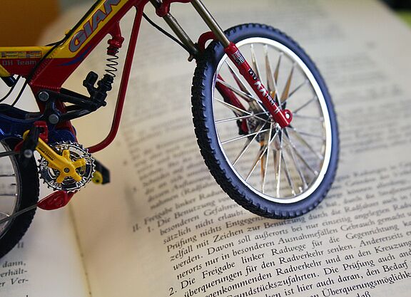 Deutscher Gesetzestext mit Fahrradbezug Miniatur-Fahrrad steht auf einem aufgeschlagenen Buch mit deutschem Gesetzestext.