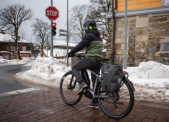Ein Mann steht mit Fahrrad an einer Ampel in winterlicher Stadtlandschaft. 